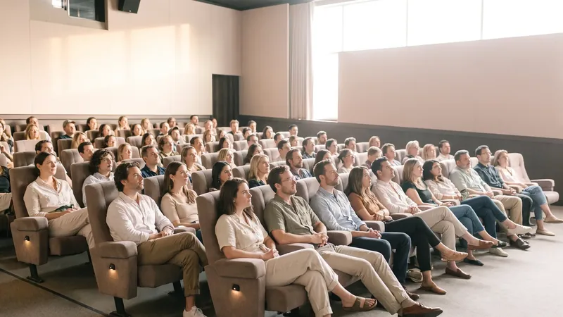 A cinema audience in rows of seats lit by the glow of the screen